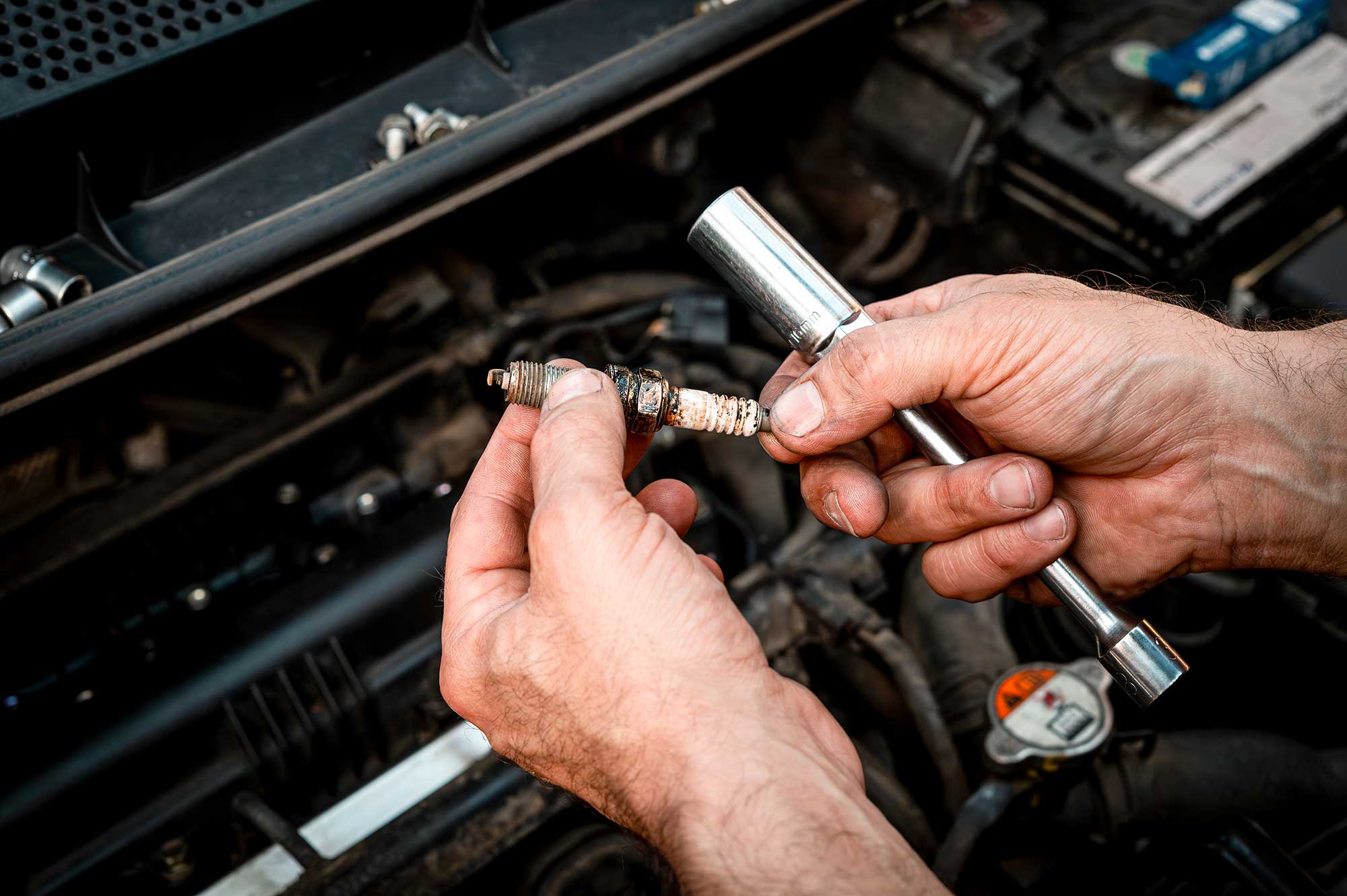 Mechanic checking spark plugs during a car tune-up service to correct rough engine idling.
