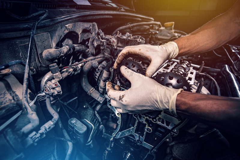 A mechanic is working on an engine, using gloves to handle components. The focus is on the intricate parts of the engine, highlighting automotive repair.